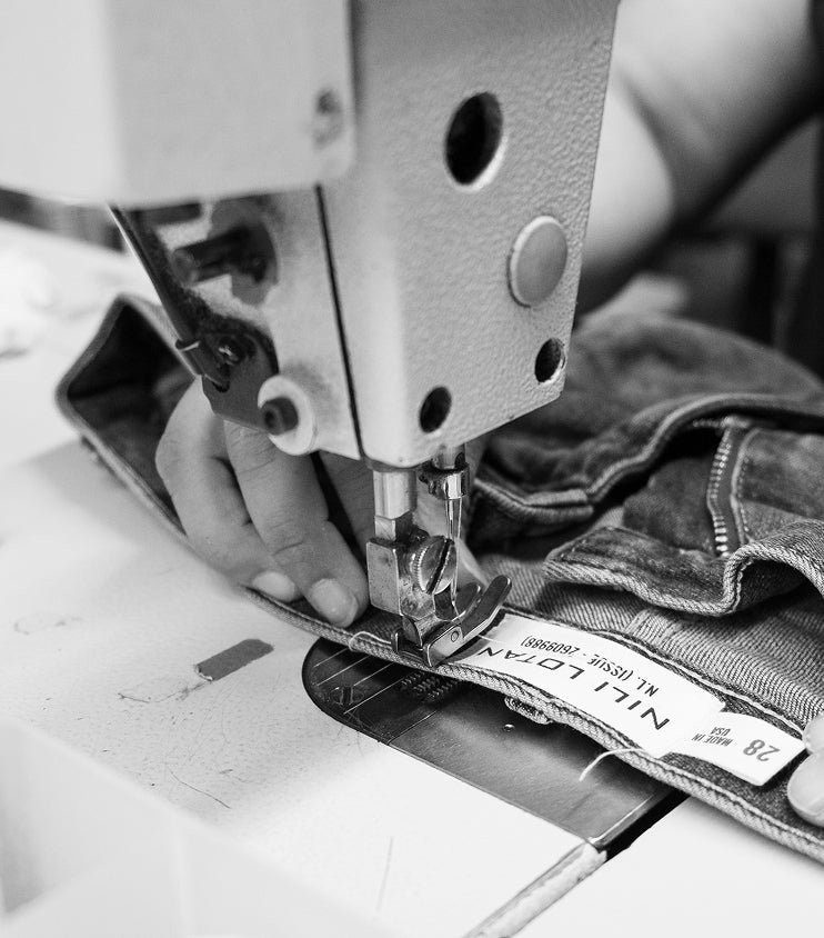 A person sewing denim fabric with a sewing machine in black and white.