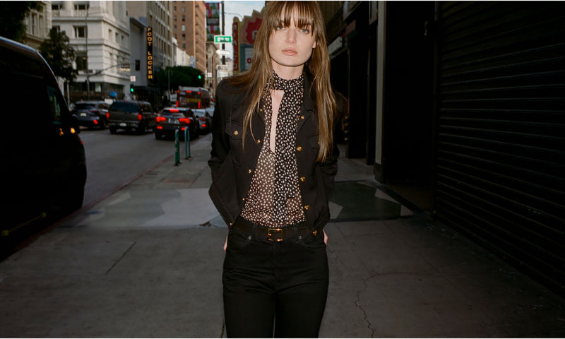 A person in a city street wearing a dark outfit and standing casually.