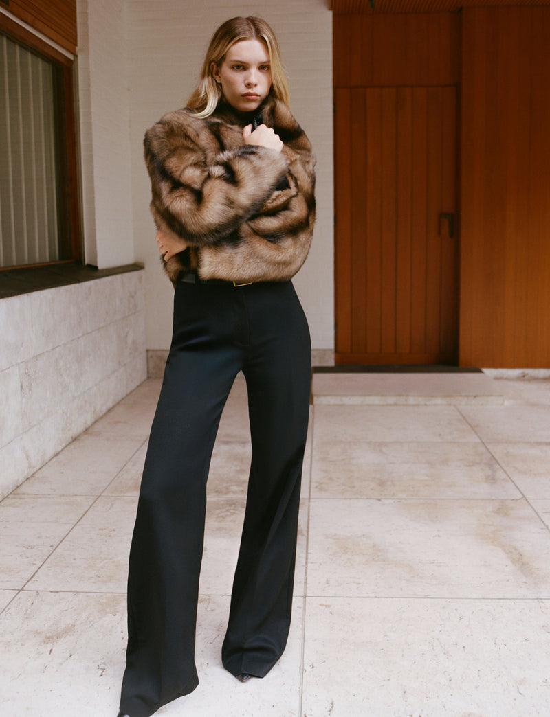 Woman in fur coat and black pants posing indoors.