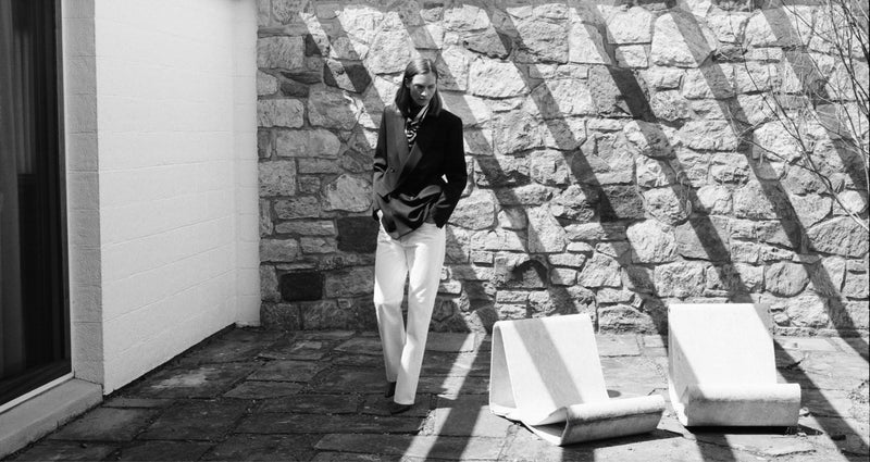 Person in black and white outfit stands near stone wall and loungers.